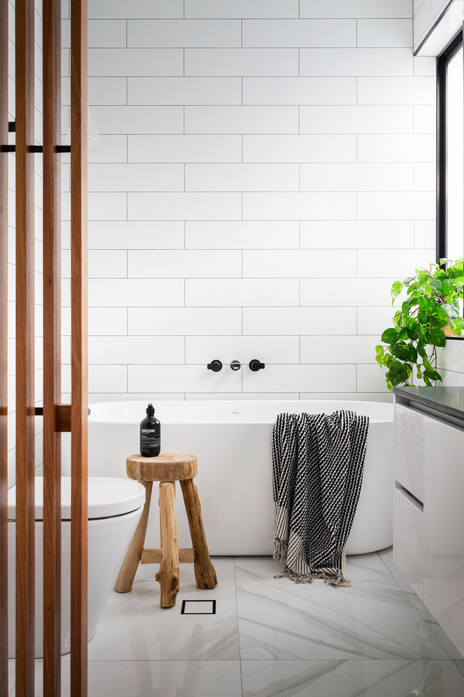 Inspiration for a mid-sized contemporary master bathroom in Canberra - Queanbeyan with white cabinets, a freestanding tub, an open shower, a one-piece toilet, white tile, subway tile, white walls, porcelain floors, a vessel sink, engineered quartz benchtops, white floor, an open shower, black benchtops and flat-panel cabinets.