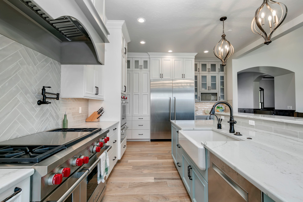 Example of a large country l-shaped light wood floor and beige floor kitchen design in Boise with a farmhouse sink, recessed-panel cabinets, white cabinets, gray backsplash, stainless steel appliances and white countertops