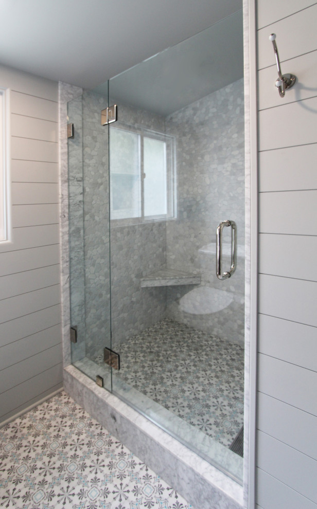 Design ideas for a small beach style 3/4 bathroom in Other with furniture-like cabinets, medium wood cabinets, an alcove shower, a two-piece toilet, gray tile, pebble tile, grey walls, marble floors, an undermount sink, marble benchtops, multi-coloured floor, a hinged shower door, white benchtops, a shower seat, a single vanity, a freestanding vanity and planked wall panelling.