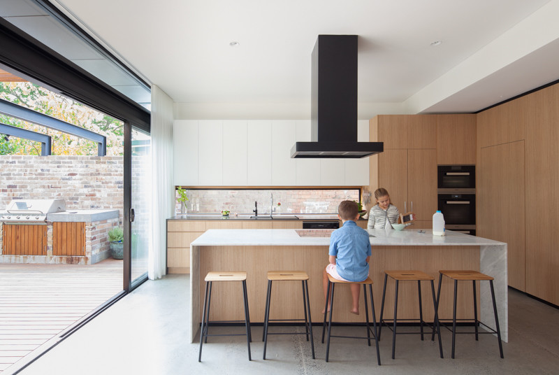 Inspiration for a mid-sized contemporary l-shaped open plan kitchen in Sydney with a double-bowl sink, light wood cabinets, marble benchtops, window splashback, black appliances, concrete floors and with island.