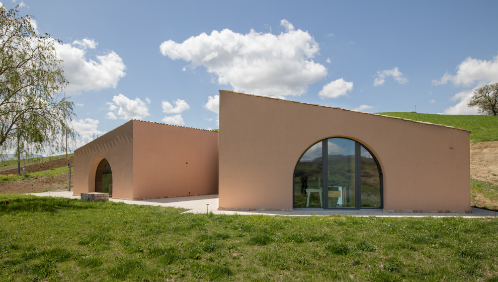 Cette image montre une grande façade de maison rose design en béton avec un toit en appentis et un toit en tuile.