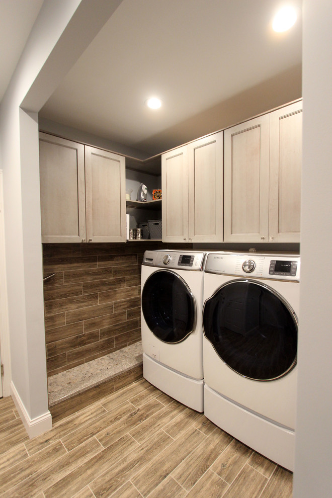 Mid-sized transitional galley utility room in Cleveland with flat-panel cabinets, grey cabinets, grey walls, laminate floors, a side-by-side washer and dryer and brown floor.