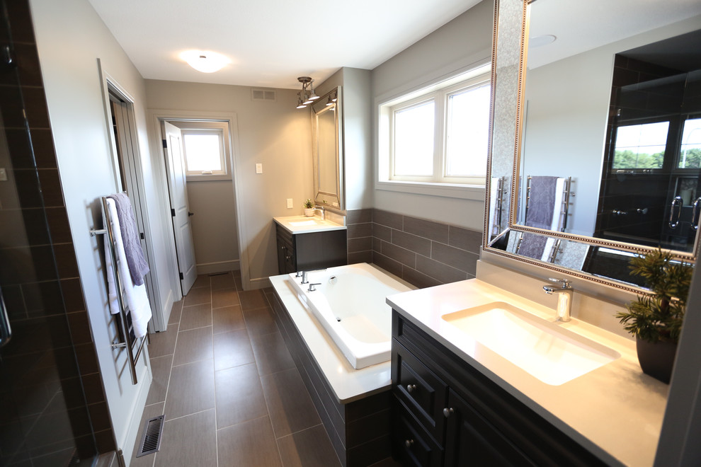 This is an example of a mid-sized traditional master bathroom in Other with raised-panel cabinets, dark wood cabinets, a drop-in tub, an alcove shower, a two-piece toilet, gray tile, porcelain tile, beige walls, porcelain floors, an undermount sink and quartzite benchtops.