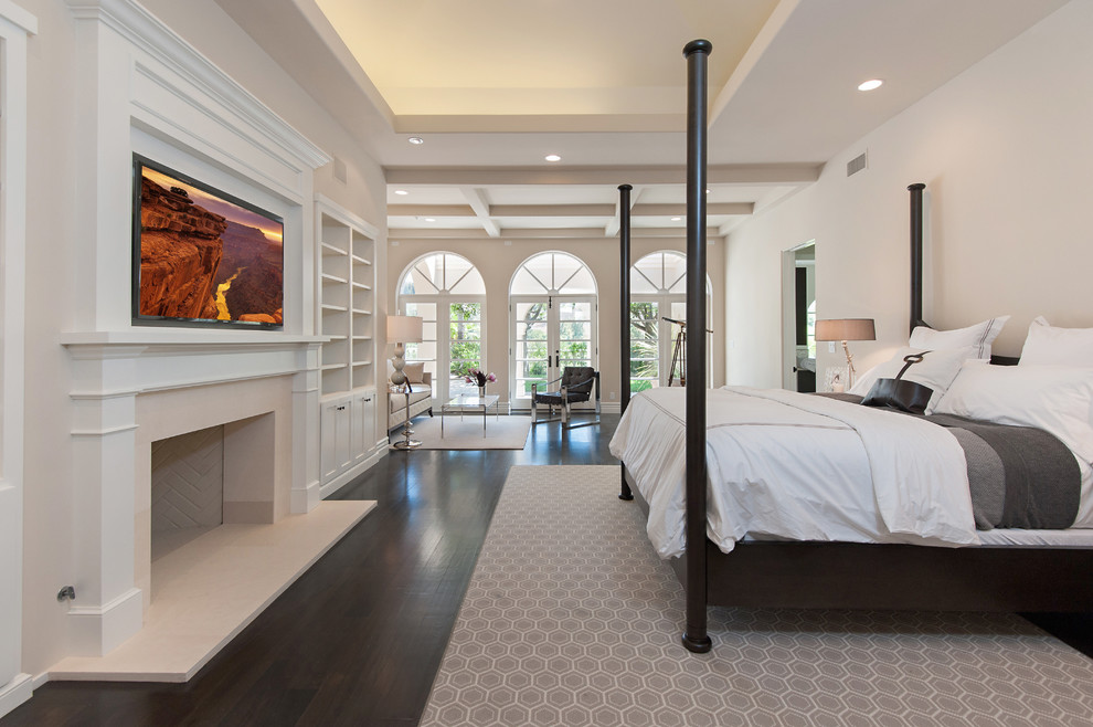 Inspiration for an expansive mediterranean master bedroom in Los Angeles with beige walls, dark hardwood floors, a standard fireplace and a plaster fireplace surround.