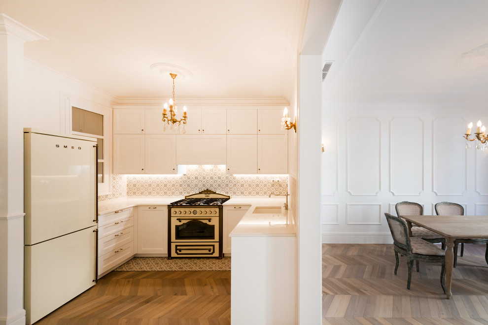 Diseño de cocinas en U tradicional de tamaño medio abierto sin isla con fregadero de un seno, armarios con paneles con relieve, puertas de armario blancas y suelo de madera en tonos medios