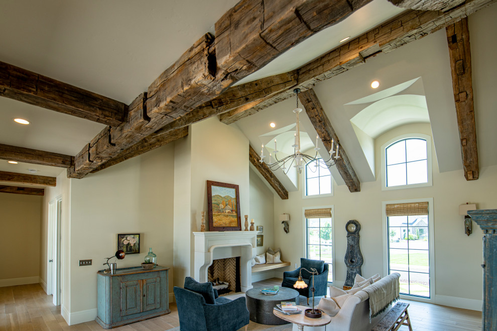 Cette image montre un grand salon ouvert avec un mur blanc, une cheminée standard, un manteau de cheminée en plâtre, aucun téléviseur, un sol beige et un plafond en bois.