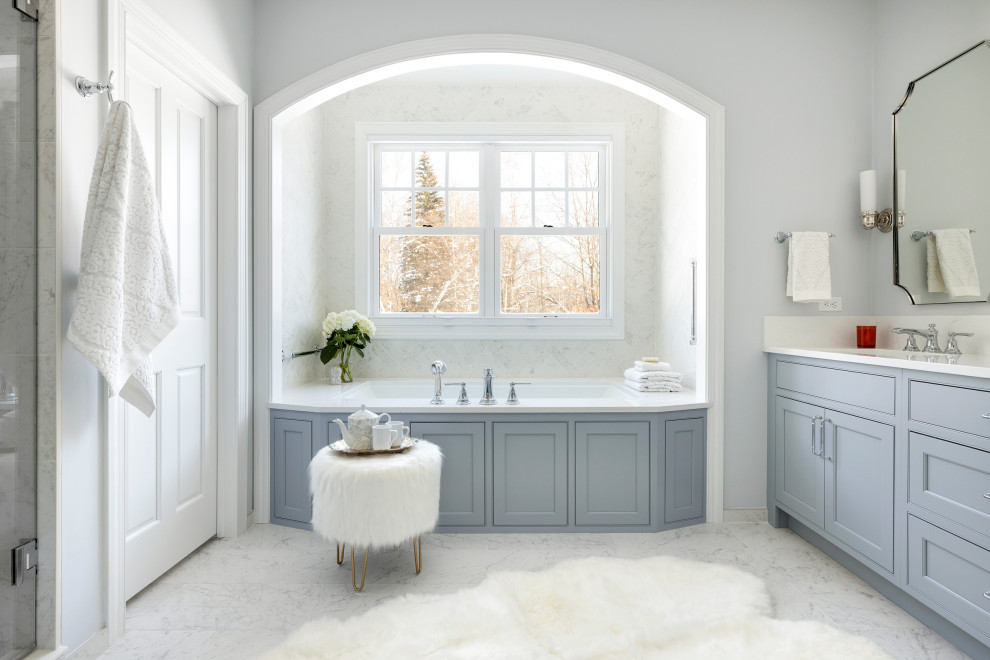 На фото: главная ванная комната с фасадами с утопленной филенкой, синими фасадами, полновстраиваемой ванной, душем в нише, раздельным унитазом, белой плиткой, мраморной плиткой, серыми стенами, мраморным полом, врезной раковиной, столешницей из искусственного кварца, белым полом, душем с распашными дверями, белой столешницей, сиденьем для душа, тумбой под две раковины и встроенной тумбой с