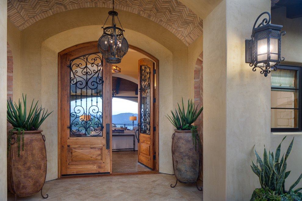 This is an example of an expansive mediterranean front door in San Diego with beige walls, limestone flooring, a double front door, a medium wood front door, beige floors, a vaulted ceiling and brick walls.
