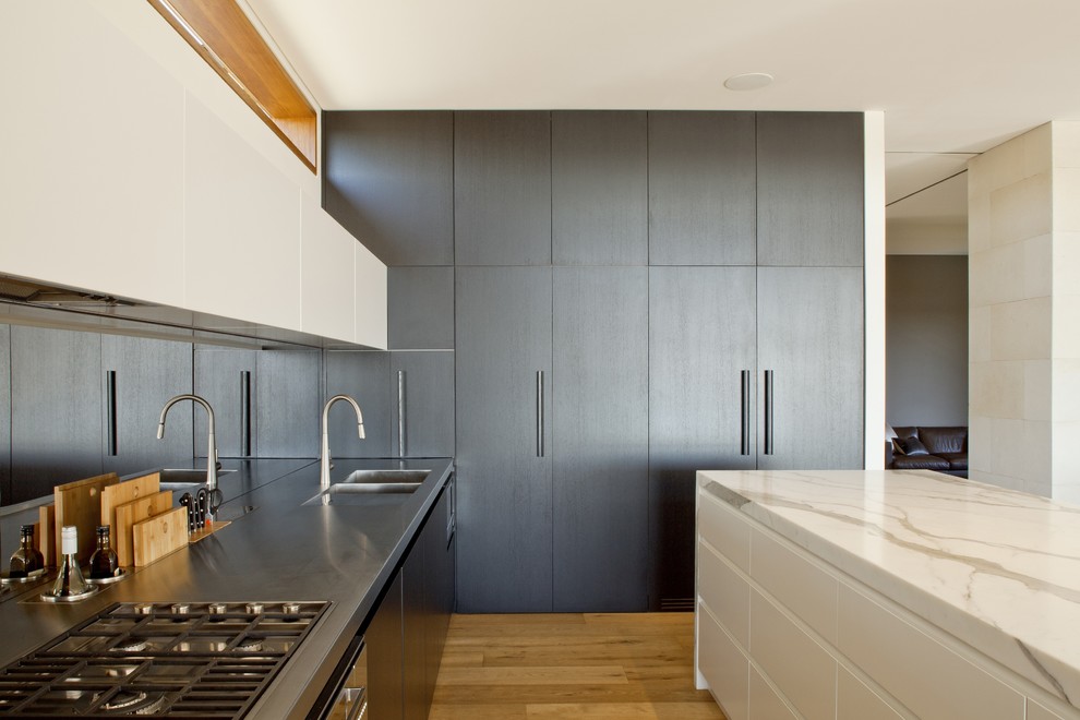 Design ideas for a large contemporary galley open plan kitchen in Sydney with a double-bowl sink, flat-panel cabinets, dark wood cabinets, marble benchtops, mirror splashback, stainless steel appliances, medium hardwood floors and with island.