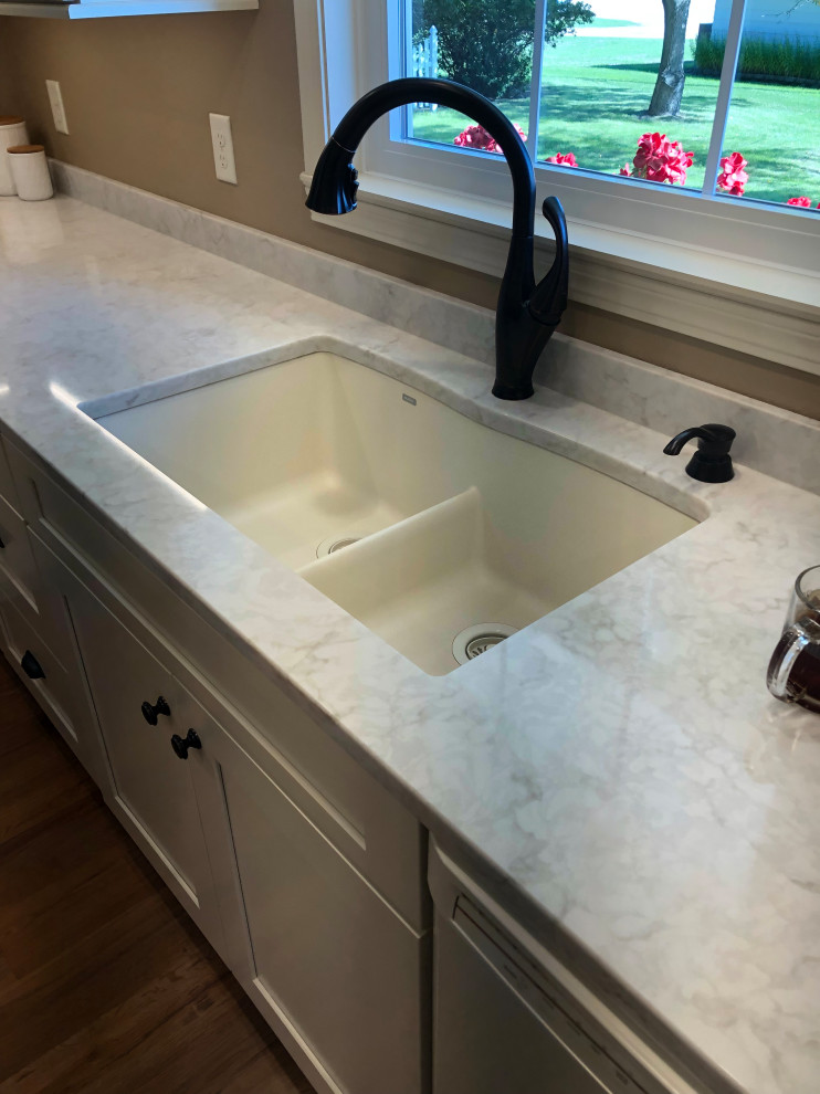 Photo of a mid-sized traditional galley separate kitchen in Other with a double-bowl sink, flat-panel cabinets, beige cabinets, quartzite benchtops, white appliances, laminate floors, no island, brown floor and white benchtop.