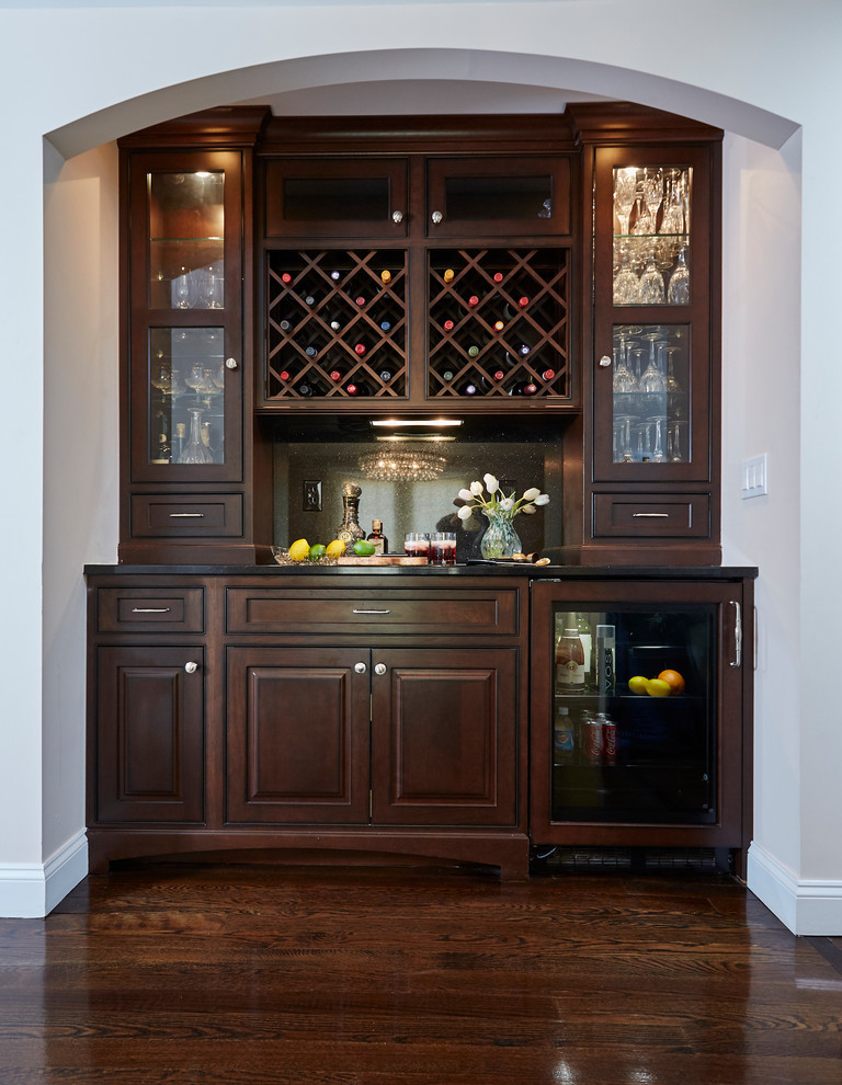 Photo of a traditional home bar in New York with raised-panel cabinets, dark wood cabinets, dark hardwood floors and brown floor.