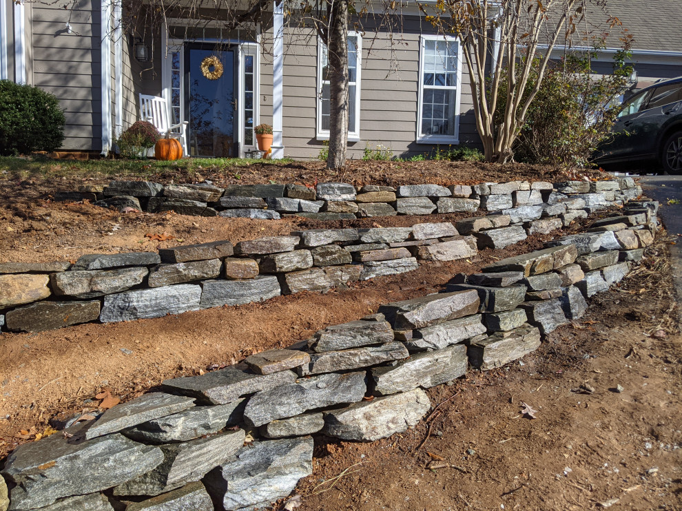 This is an example of a large midcentury front yard partial sun driveway in Richmond with a retaining wall, natural stone pavers and a stone fence.