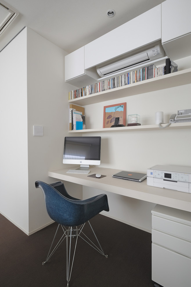 This is an example of a small modern study room in Tokyo with white walls, carpet, no fireplace, a built-in desk and brown floor.