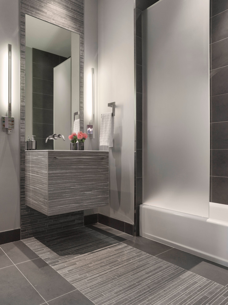 Inspiration for a mid-sized contemporary bathroom in San Francisco with flat-panel cabinets, grey cabinets, a drop-in tub, a shower/bathtub combo, a one-piece toilet, gray tile, ceramic tile, grey walls, ceramic floors, solid surface benchtops, grey floor and an integrated sink.