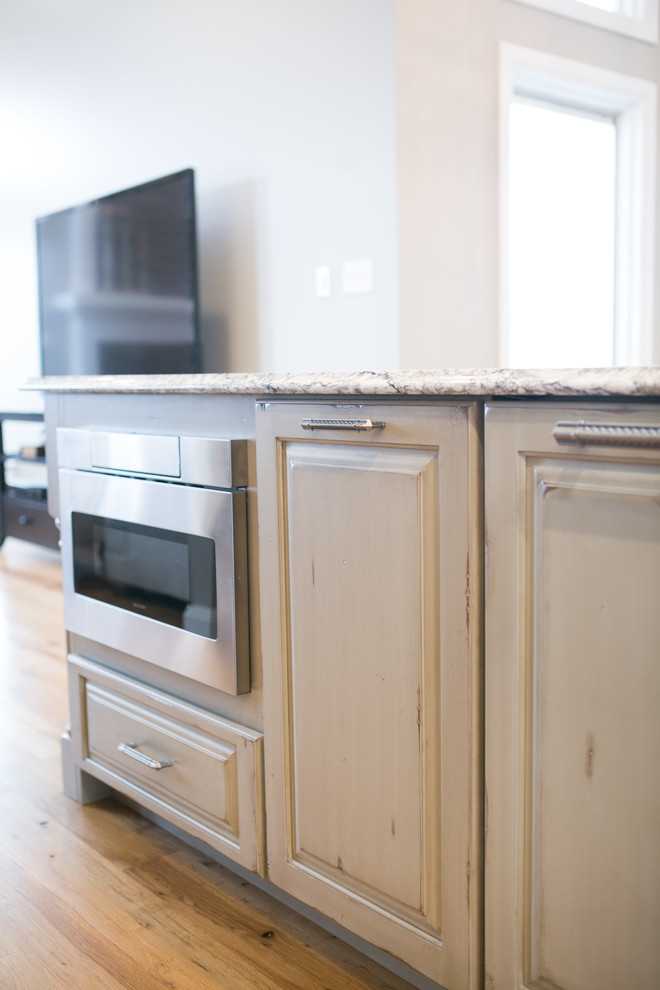 Example of a large transitional u-shaped medium tone wood floor and brown floor kitchen design in Indianapolis with a farmhouse sink, raised-panel cabinets, dark wood cabinets, granite countertops, white backsplash, subway tile backsplash, paneled appliances, an island and multicolored countertops