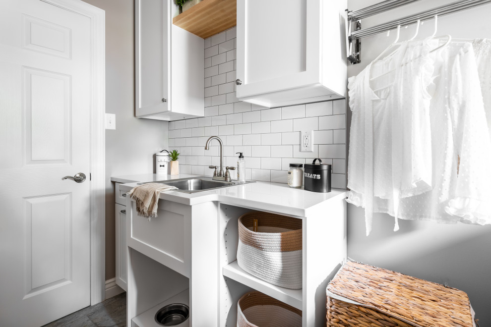 This is an example of a small beach style single-wall utility room in St Louis with a drop-in sink, flat-panel cabinets, white cabinets, wood benchtops, white splashback, subway tile splashback, grey walls, porcelain floors, a side-by-side washer and dryer, grey floor and multi-coloured benchtop.