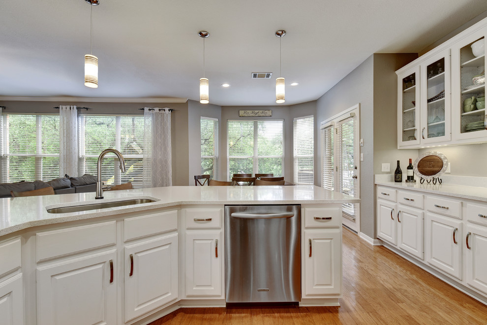 Example of a mid-sized transitional u-shaped light wood floor eat-in kitchen design in Austin with an undermount sink, white cabinets, quartz countertops, white backsplash, stone slab backsplash, stainless steel appliances, a peninsula and raised-panel cabinets