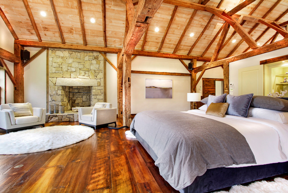На фото: огромная хозяйская спальня в стиле рустика с белыми стенами, паркетным полом среднего тона, стандартным камином, фасадом камина из каменной кладки, сводчатым потолком и деревянными стенами с