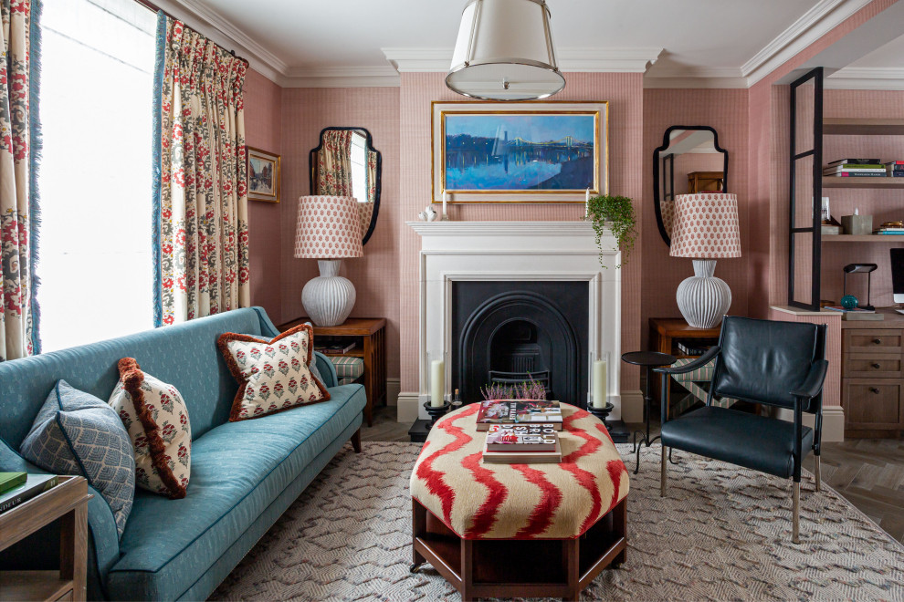 This is an example of a transitional formal open concept living room in London with pink walls, medium hardwood floors, a standard fireplace, no tv, brown floor and wallpaper.