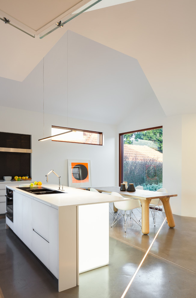Contemporary kitchen in Sydney with a drop-in sink, flat-panel cabinets, white cabinets, quartz benchtops, grey splashback, ceramic splashback, stainless steel appliances, concrete floors and with island.