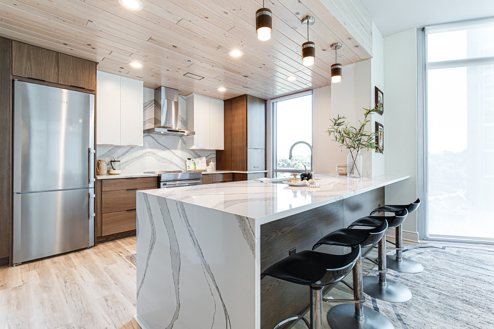 Photo of a mid-sized contemporary galley open plan kitchen in Atlanta with an undermount sink, flat-panel cabinets, brown cabinets, quartz benchtops, white splashback, engineered quartz splashback, stainless steel appliances, vinyl floors, with island, beige floor, white benchtop and wood.