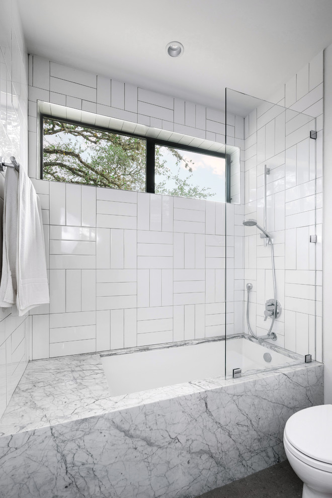Mid-sized modern master bathroom in Austin with flat-panel cabinets, medium wood cabinets, a corner tub, an alcove shower, a two-piece toilet, white tile, stone tile, white walls, concrete floors, an undermount sink, marble benchtops, grey floor and a hinged shower door.