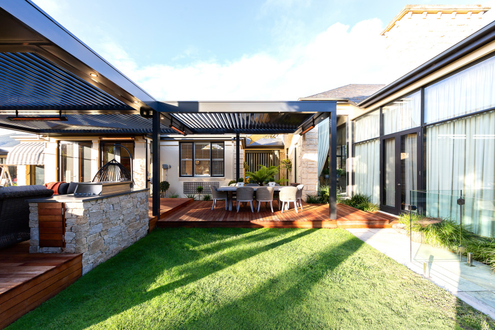 This is an example of a large contemporary backyard verandah in Melbourne with with fireplace, decking and a pergola.