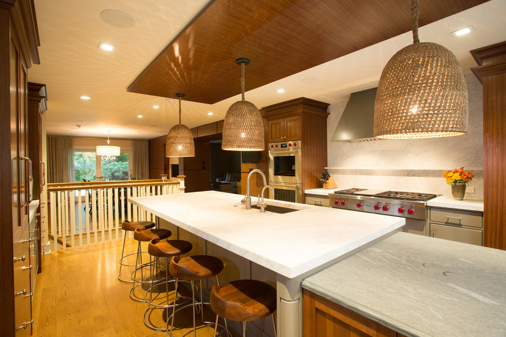 Idée de décoration pour une cuisine parallèle design de taille moyenne avec un évier encastré, une crédence blanche, un électroménager en acier inoxydable, un sol en bois brun, îlot et un plan de travail blanc.