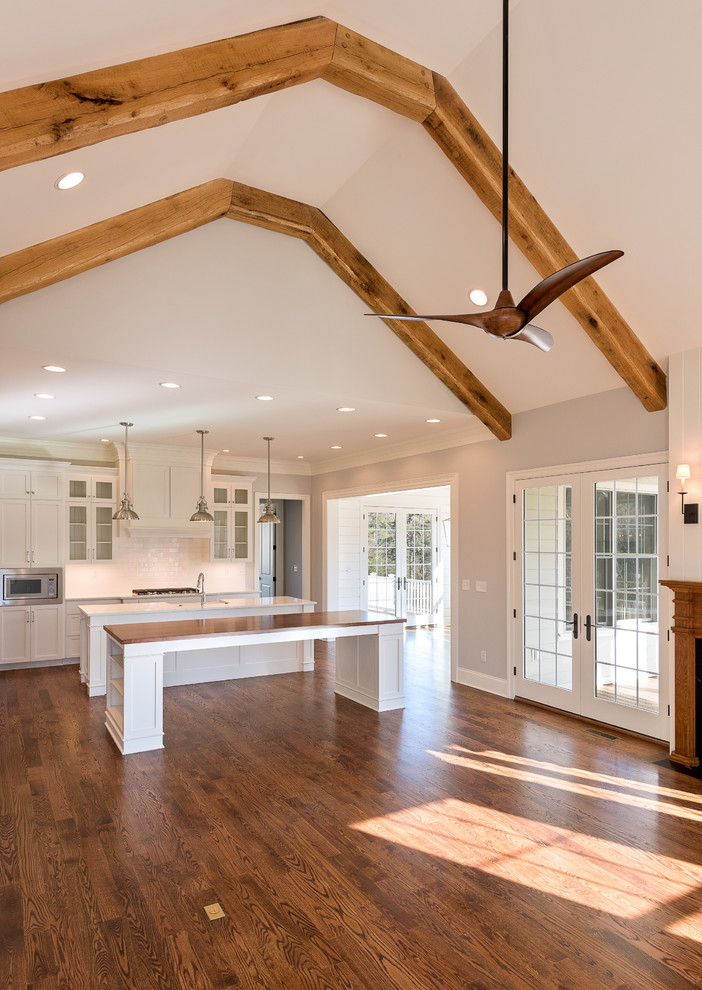 Example of a mid-sized transitional l-shaped dark wood floor and brown floor open concept kitchen design with a farmhouse sink, shaker cabinets, white cabinets, granite countertops, stainless steel appliances and two islands