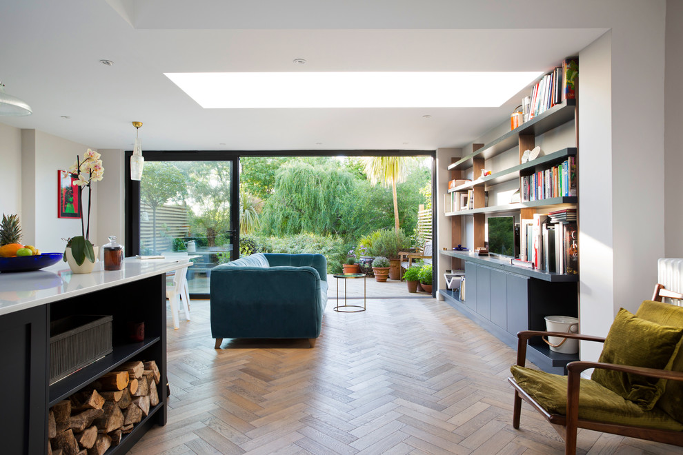 This is an example of a mid-sized transitional open concept living room in London with a library, white walls, light hardwood floors, no fireplace and a built-in media wall.