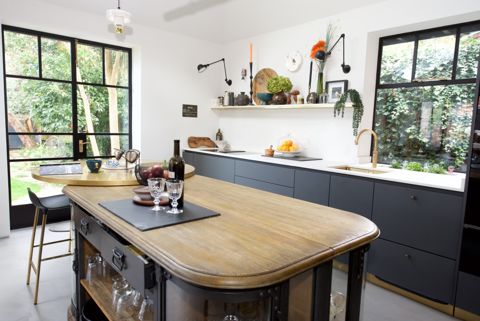 Inspiration for a large contemporary open plan kitchen in London with a double-bowl sink, flat-panel cabinets, black cabinets, quartz benchtops, white splashback, engineered quartz splashback, black appliances, concrete floors, with island, grey floor, white benchtop and exposed beam.