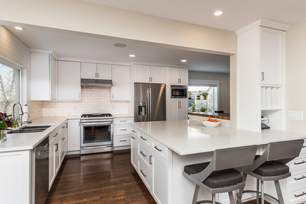 Eat-in kitchen - mid-sized transitional dark wood floor eat-in kitchen idea in Denver with an undermount sink, shaker cabinets, white cabinets, quartz countertops, white backsplash, porcelain backsplash, stainless steel appliances, an island and white countertops