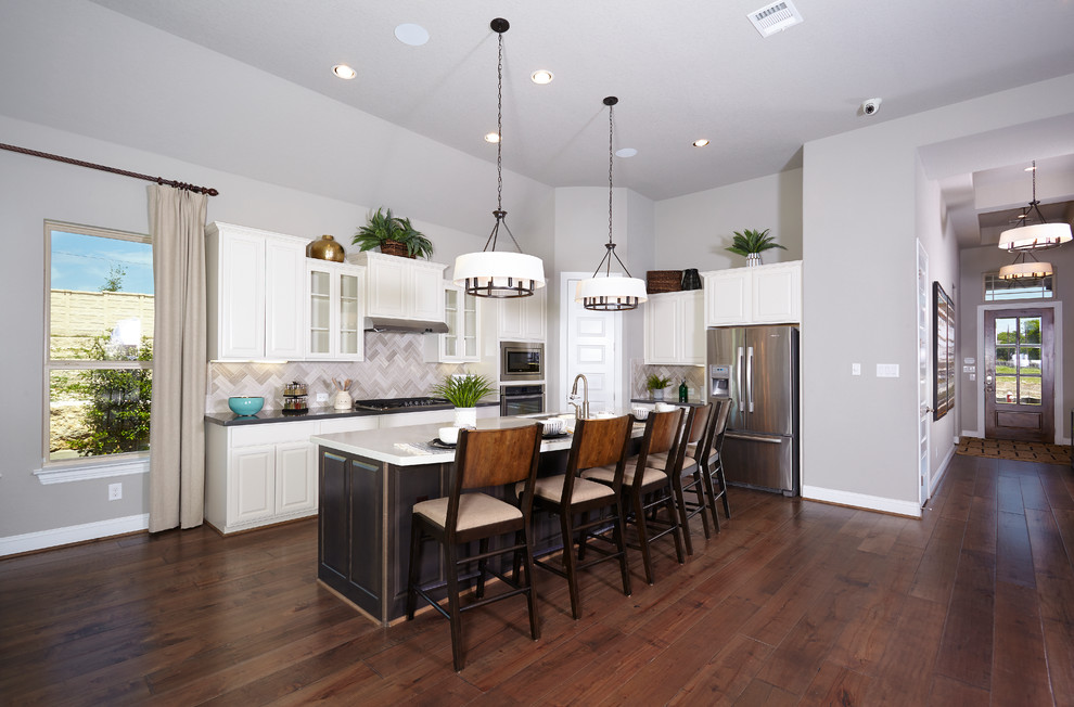 Large l-shaped eat-in kitchen in Austin with a double-bowl sink, raised-panel cabinets, white cabinets, quartzite benchtops, grey splashback, stone tile splashback, stainless steel appliances, dark hardwood floors, with island and brown floor.
