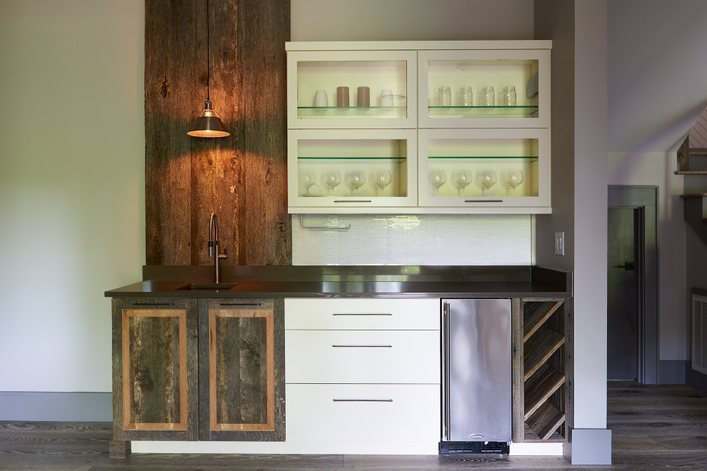 Inspiration for a contemporary wet bar in Other with an undermount sink, recessed-panel cabinets, brown cabinets, wood benchtops, white splashback, ceramic splashback, light hardwood floors, grey floor and black benchtop.