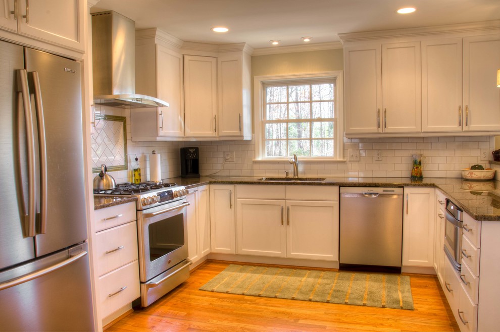 This is an example of a traditional u-shaped eat-in kitchen in Raleigh with an undermount sink, raised-panel cabinets, granite benchtops, white splashback, subway tile splashback and stainless steel appliances.