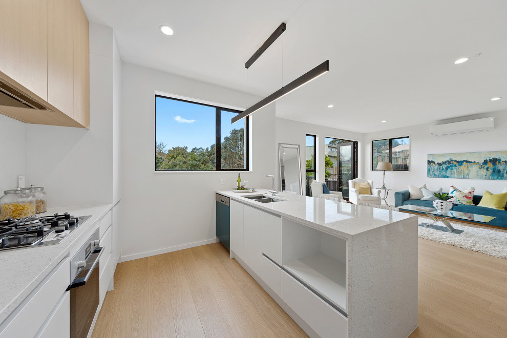 Inspiration for a contemporary kitchen in Auckland with an undermount sink, light wood cabinets, quartz benchtops, white splashback, glass sheet splashback, stainless steel appliances, laminate floors, with island and white benchtop.