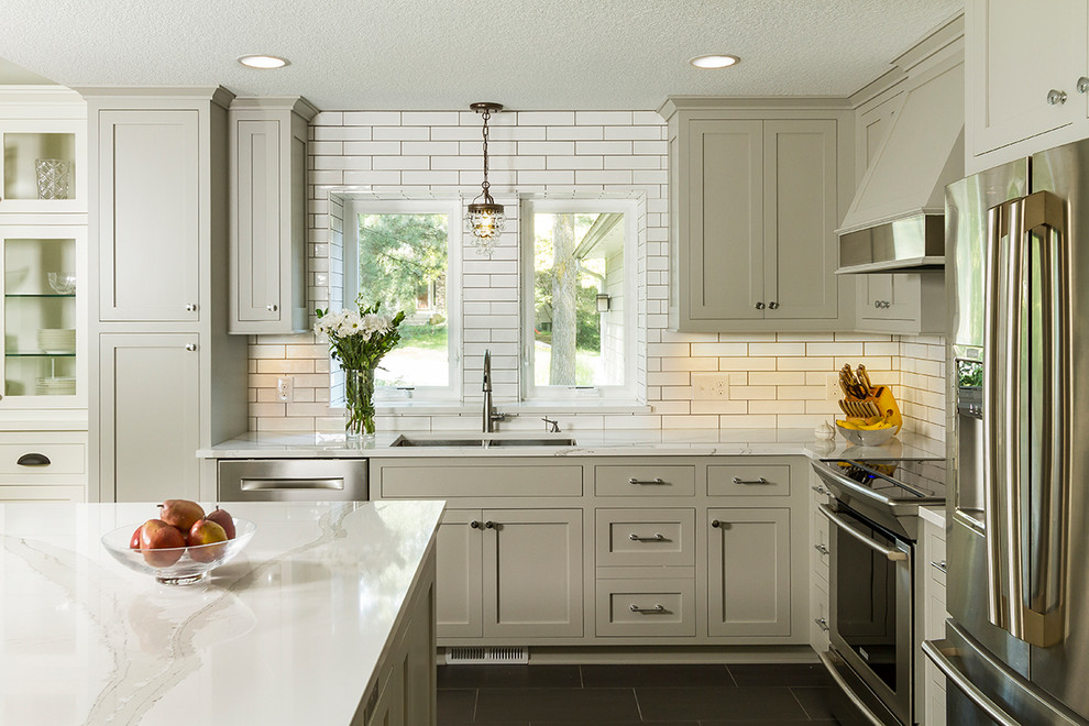 Photo of a mid-sized traditional l-shaped kitchen in Minneapolis with an undermount sink, shaker cabinets, grey cabinets, quartz benchtops, white splashback, stainless steel appliances, with island, black floor and subway tile splashback.