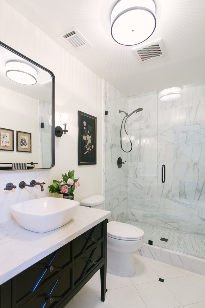 This is an example of a mid-sized country 3/4 bathroom in Santa Barbara with furniture-like cabinets, black cabinets, an alcove shower, a two-piece toilet, white walls, porcelain floors, a vessel sink, marble benchtops, white floor, a hinged shower door and white benchtops.