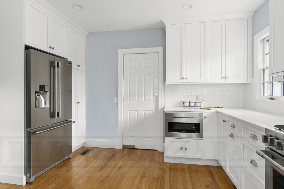 Enclosed kitchen - mid-sized transitional u-shaped medium tone wood floor enclosed kitchen idea in Providence with a farmhouse sink, shaker cabinets, white cabinets, quartz countertops, white backsplash, ceramic backsplash, stainless steel appliances, no island and white countertops