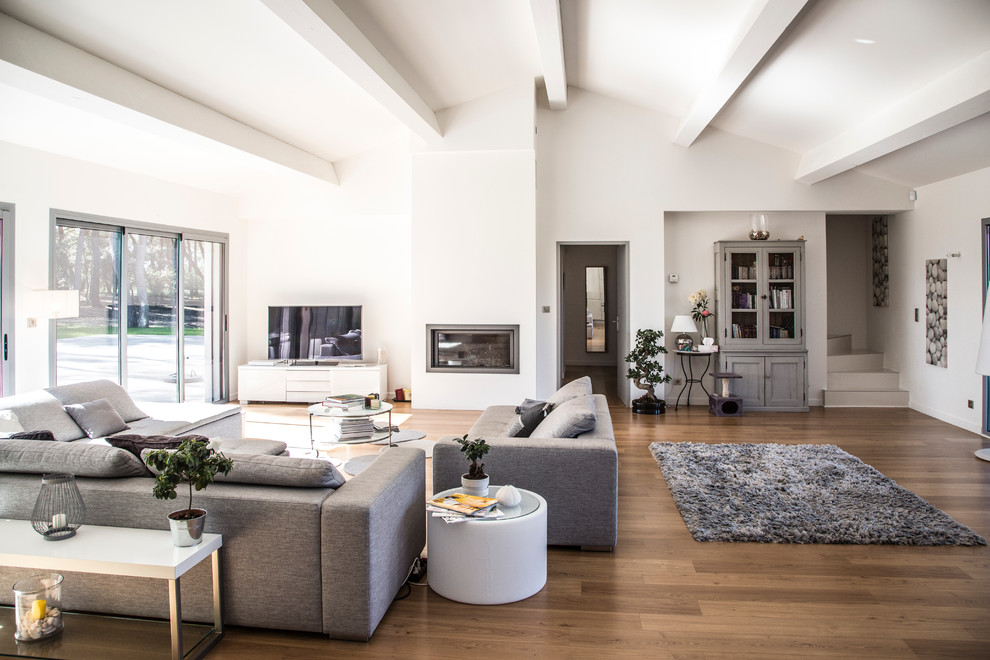 Inspiration for a large contemporary open concept family room in Marseille with white walls, medium hardwood floors, a ribbon fireplace, a freestanding tv and a library.