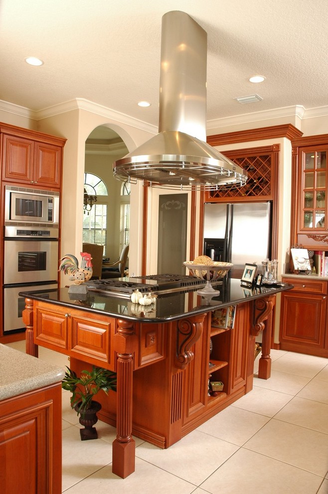 This is an example of a traditional kitchen in Los Angeles with stainless steel appliances, raised-panel cabinets, medium wood cabinets, marble benchtops, porcelain floors and with island.