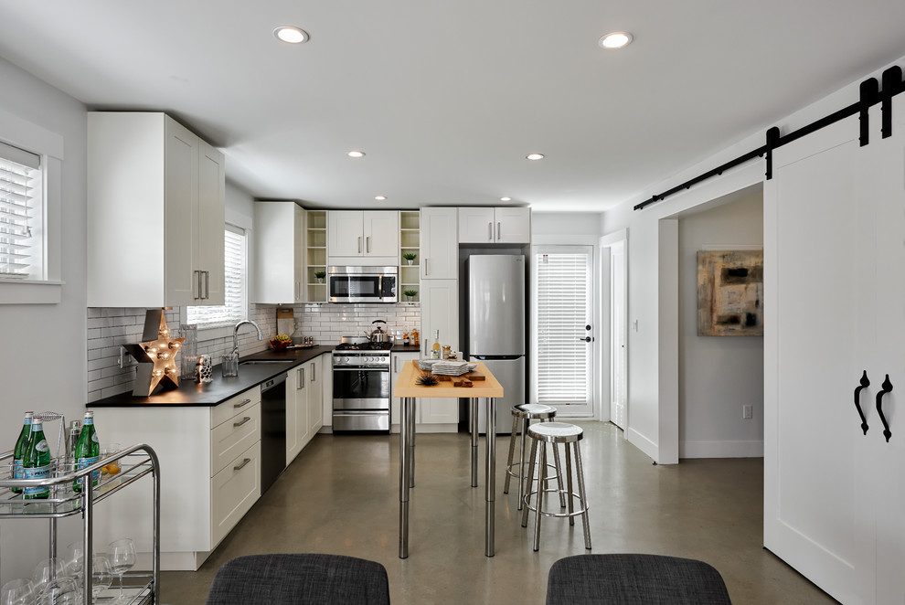 Eat-in kitchen - transitional l-shaped concrete floor eat-in kitchen idea in Vancouver with an undermount sink, shaker cabinets, white cabinets, white backsplash, subway tile backsplash, stainless steel appliances and an island