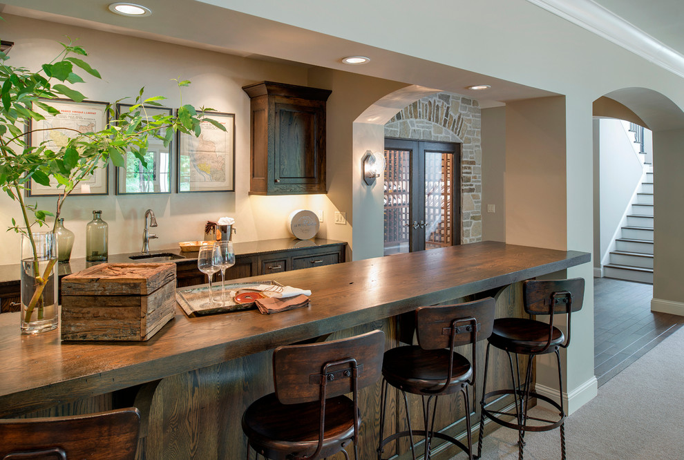 Design ideas for a mid-sized mediterranean galley seated home bar in Minneapolis with an undermount sink, recessed-panel cabinets, dark wood cabinets, wood benchtops, dark hardwood floors and brown benchtop.
