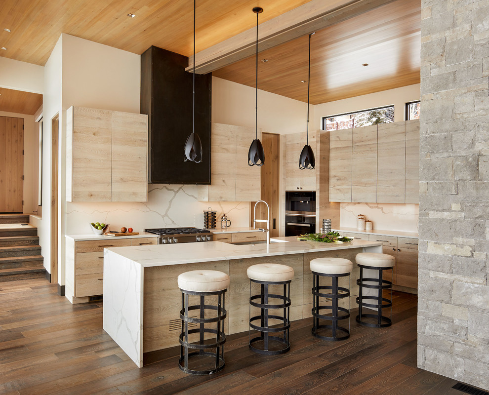 Example of a large mountain style l-shaped medium tone wood floor and brown floor open concept kitchen design in Denver with a farmhouse sink, flat-panel cabinets, light wood cabinets, marble countertops, white backsplash, marble backsplash, stainless steel appliances, an island and white countertops