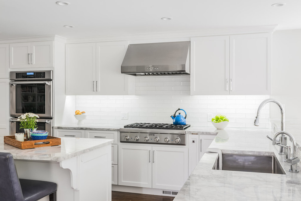 Large transitional u-shaped open plan kitchen in Boston with an undermount sink, shaker cabinets, white cabinets, marble benchtops, white splashback, subway tile splashback, stainless steel appliances, dark hardwood floors, with island, brown floor and grey benchtop.