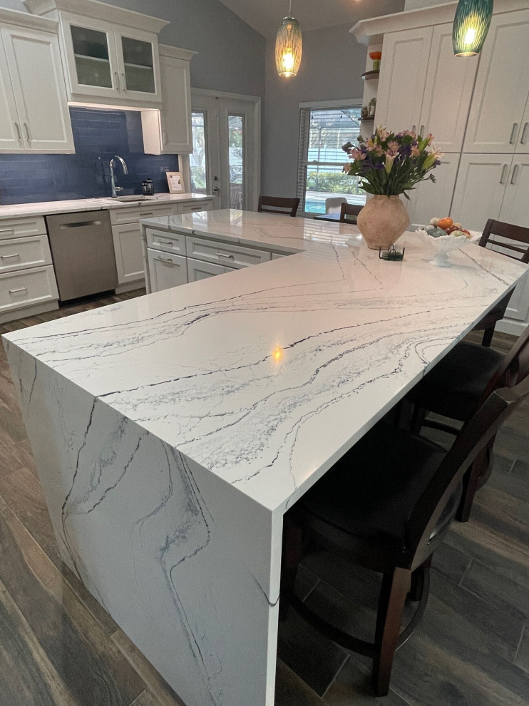 Mid-sized transitional l-shaped eat-in kitchen in Tampa with shaker cabinets, white cabinets, quartz benchtops, glass tile splashback and with island.