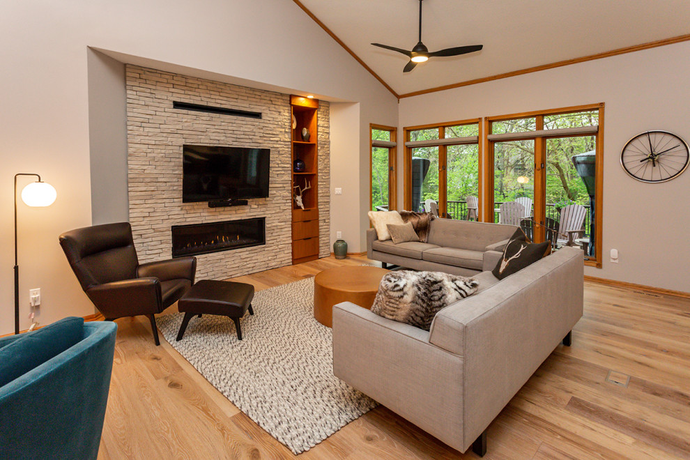 Photo of a large contemporary open concept living room in Other with grey walls, light hardwood floors, a standard fireplace, a stone fireplace surround, a wall-mounted tv, beige floor and vaulted.
