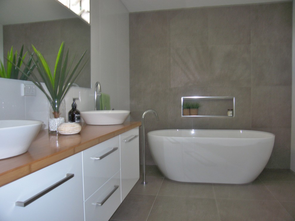 Inspiration for a large master bathroom in Sydney with white cabinets, a freestanding tub, an open shower, a one-piece toilet, beige tile, ceramic tile, white walls, porcelain floors, a vessel sink and wood benchtops.