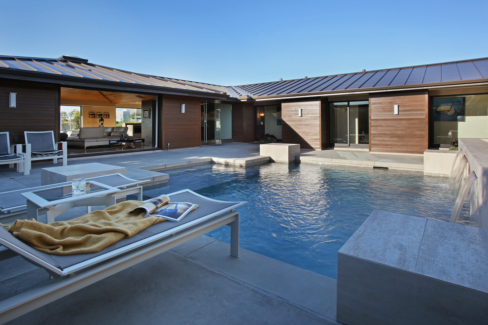 Inspiration for a mid-sized modern courtyard custom-shaped pool in Orange County with a water feature and concrete slab.