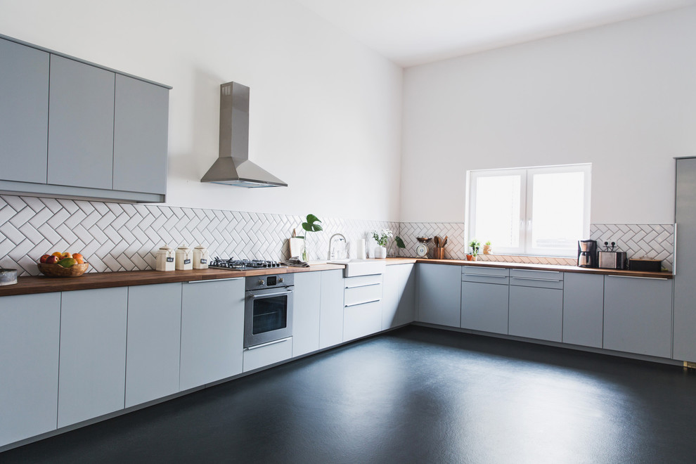 Design ideas for a mid-sized scandinavian open plan kitchen in Berlin with a farmhouse sink, grey cabinets, wood benchtops, white splashback, ceramic splashback, stainless steel appliances, concrete floors and no island.